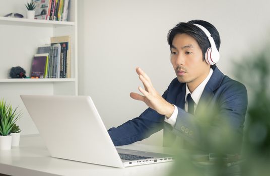 Asian Businessman or Asian Consultant in Formal Navy Blue Suit Talking and Suggest Customer on Laptop Screen in Office. Consulting services from professional consultant