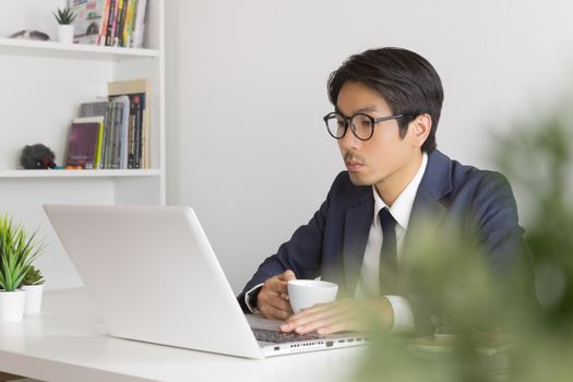 Asian Businessman Wear Eyeglasses Seriously Analyze Financial Data in Laptop. Asian businessman working in office