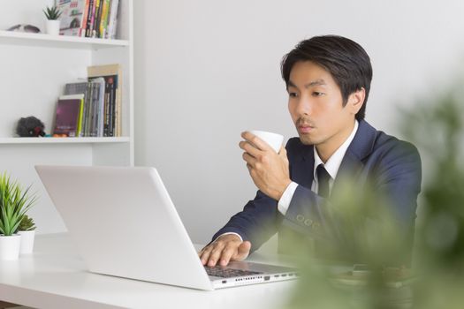 Asian Businessman with White Coffee Cup in Left Hand with Tree Foreground in Office. Relax time for Asian businessman