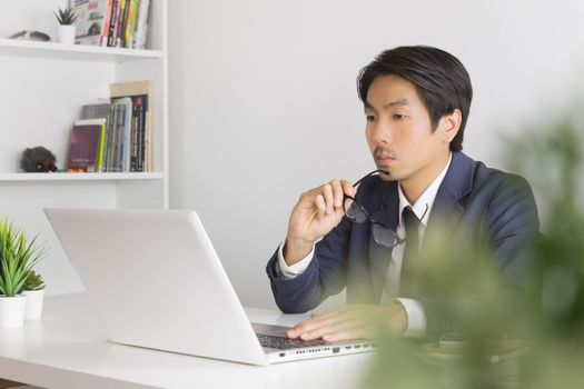 Asian Financial Advisor or Asian Consulting Businessman Serious with Financial Information in front of Laptop. Asian financial advisor or Asian consulting businessman working in office