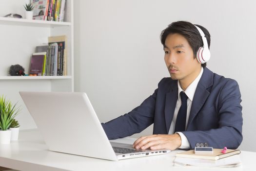 Asian Man Call Center in Suit Wear Headset or Headphone Contacting and Service the Customer Via Internet in Office. Asian man call center working with laptop