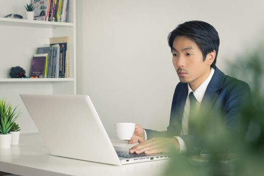 Asian Businessman with White Coffee Cup in Break Time with Tree Foreground in Office. Relax time for Asian businessman