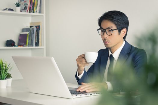 Asian Businessman Wear Eyeglasses with Coffee Cup and Tree Foreground in Office. Relax time for Asian businessman