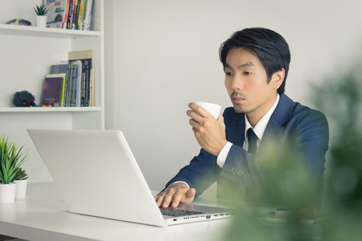 Asian Businessman with White Coffee Cup in Left Hand with Tree Foreground in Office. Relax time for Asian businessman