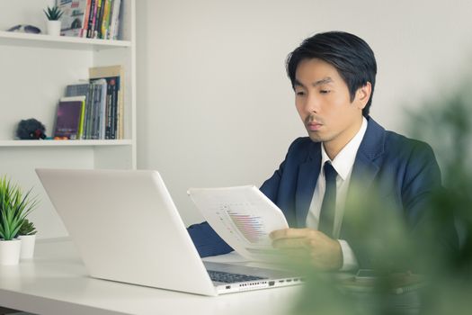 Asian Financial Advisor or Asian Consulting Businessman Analyze Financial Report in front of Laptop. Asian financial advisor or Asian consulting businessman working in office