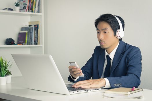 Asian Man Call Center in Suit Wear Headset Answer Customer Questions by Smartphone and Laptop. Asian man call center working in Office