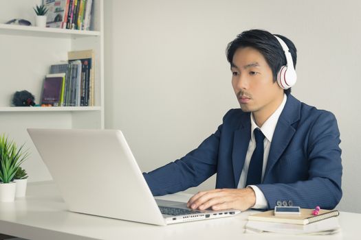Asian Man Call Center in Suit Wear Headset or Headphone Contacting and Service the Customer Via Internet in Office. Asian man call center working with laptop