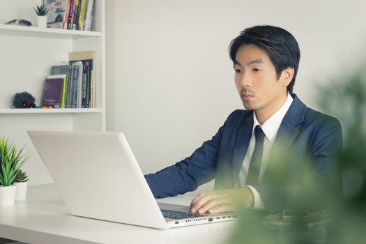 Asian Businessman In front of Laptop Monitor and Tree Foreground. Asian businessman working in office