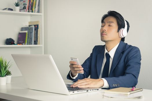 Asian Businessman in Suit Wear Headphone Listen to Music by Bluetooth Technology in Smartphone. Relax time of Asian businessman in office