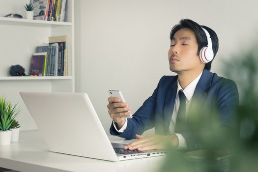 Asian Businessman Listen to Music by Headphone with Tree Foreground. Relax time of Asian businessman in office