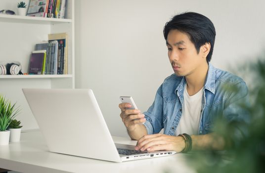 Portrait Asian Casual Businessman in Denim or Jeans Shirt Sending Message to Colleague by Smartphone in Home Office. Casual businessman working with technology