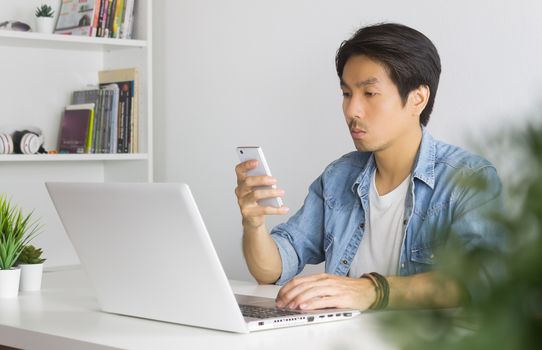 Portrait Asian Casual Businessman in Denim or Jeans Shirt Checking Mail and Chat with Colleague by Smartphone in Home Office. Casual businessman working with technology