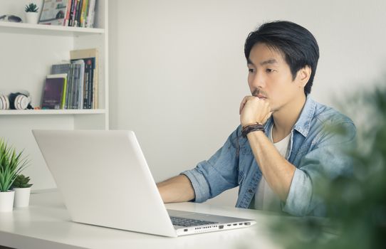 Portrait Asian Casual Businessman in Denim or Jeans Shirt Use Laptop and Thinking and Serious Pose in Home Office. Casual businessman working with technology