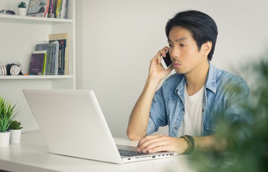 Portrait Asian Casual Businessman in Denim or Jeans Shirt Using Laptop and Smartphone in Home Office. Casual businessman working with technology