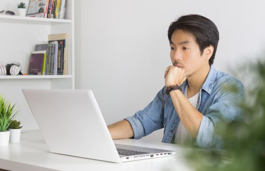 Portrait Asian Casual Businessman in Denim or Jeans Shirt Use Laptop and Thinking and Serious Pose in Home Office. Casual businessman working with technology