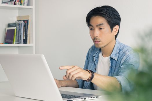 Young Asian Casual Businessman Pointing Laptop Monitor at Workplace in Home Office. Casual business or informal business in home office