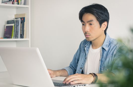 Young Asian Casual Businessman Working with Laptop at Workplace in Home Office. Casual business or informal business in home office