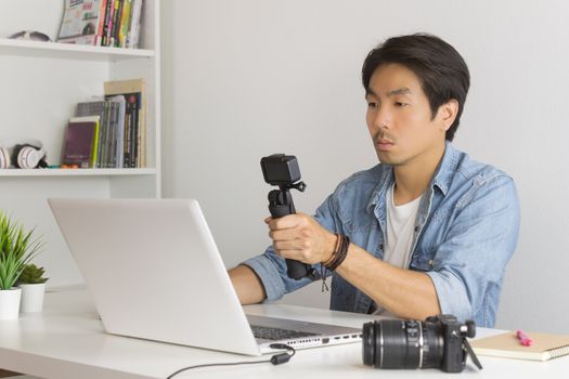 Asian Photographer or Freelancer in Denim or Jeans Shirt Selfie or Take Photo by Action Camera in Front of Laptop in Home Office. Photographer or freelancer working with technology