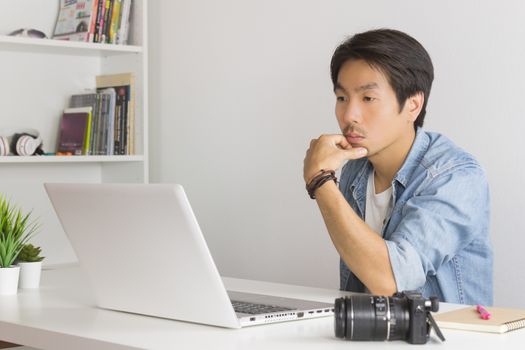 Asian Photographer or Freelancer in Denim or Jeans Shirt Serious Thinking in front of Laptop in Home Office. Photographer or freelancer working with technology