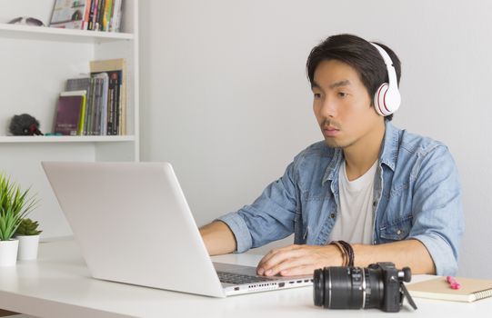Asian Freelance Videographer in Denim or Jeans Shirt Checking Multimedia Sound by Laptop in Home Office. Freelance Videographer working with technology