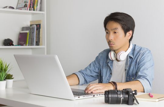 Asian Freelance Videographer in Denim or Jeans Shirt Editing Multimedia File by Laptop in Home Office. Freelance Videographer working with technology