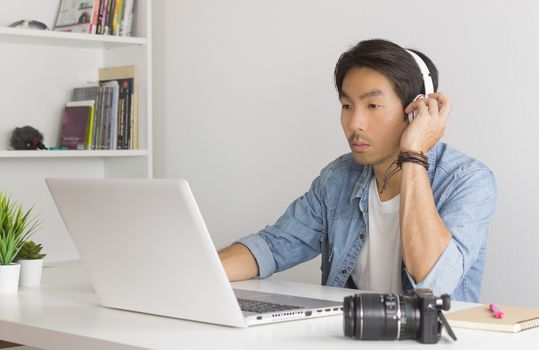 Asian Freelance Videographer in Denim or Jeans Shirt Testing Multimedia Sound by Laptop in Home Office. Freelance Videographer working with technology