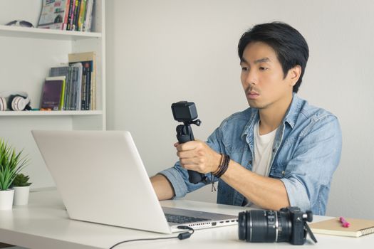 Asian Photographer or Freelancer in Denim or Jeans Shirt Selfie or Take Photo by Action Camera in Front of Laptop in Home Office. Photographer or freelancer working with technology