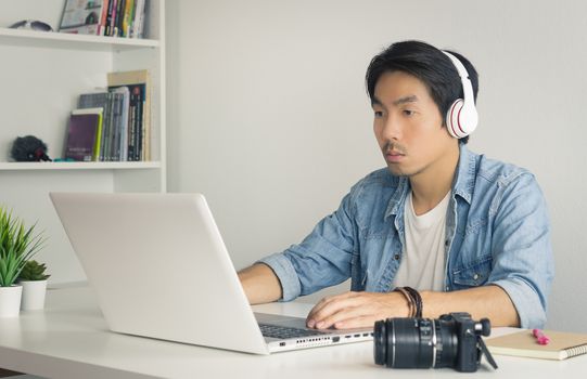 Asian Freelance Videographer in Denim or Jeans Shirt Checking Multimedia Sound by Laptop in Home Office. Freelance Videographer working with technology