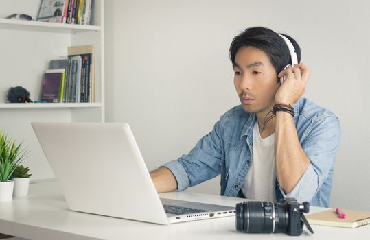 Asian Freelance Videographer in Denim or Jeans Shirt Testing Multimedia Sound by Laptop in Home Office. Freelance Videographer working with technology