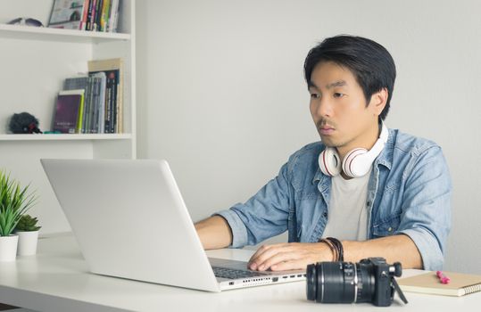 Asian Freelance Videographer in Denim or Jeans Shirt Editing Multimedia File by Laptop in Home Office. Freelance Videographer working with technology