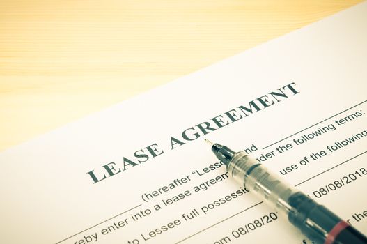 Lease agreement contract sheet and brown pen at bottom right corner on wood table background in vintage style