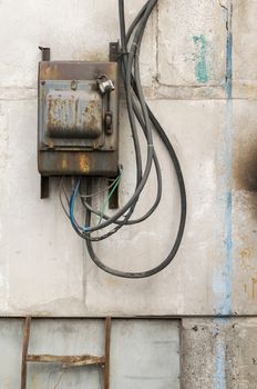 old rusty unkempt electric shield with a switch on the wall of an industrial building made of concrete blocks with molten wires sticking out of it