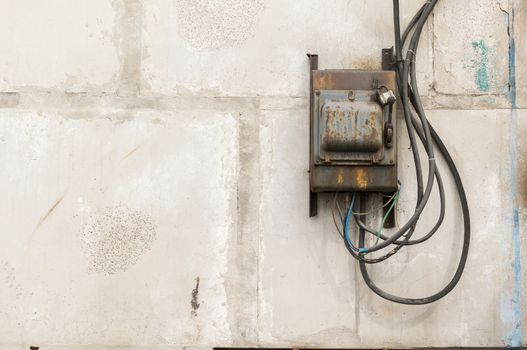 old rusty unkempt electric shield with a switch on the wall of an industrial building made of concrete blocks with molten wires sticking out of it