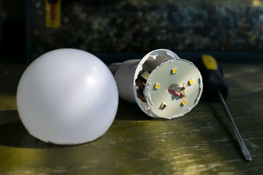 faulty, disassembled led household lamp with a burnt led element is on the table next to the screwdriver