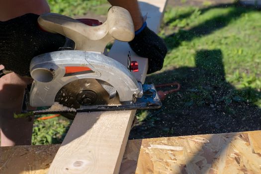 a man sawing a Board with a power tool, chips fly in all directions. Construction, wood processing