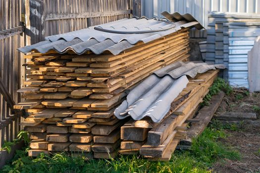 Boards, lumber, stored and covered with slate, lies in a private area in the corner of the fence on the green grass