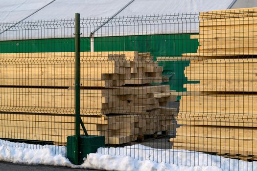 hewn, carved square logs. Lumber neatly stacked behind the fence