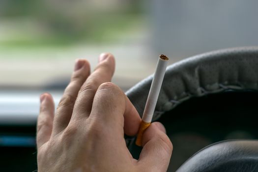 close-up, the hand of the driver of the car holds a cigarette