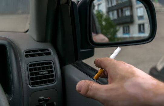 close-up of a cigarette in the hand of a man in the car, who watches the entrance door of the house