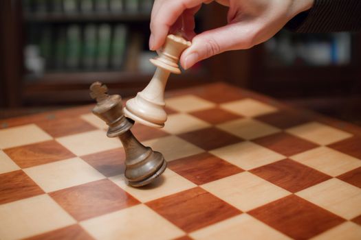 Concept: the woman who dominates the man. A woman's hand gives checkmate to the king with the queen on a wooden chessboard, with no other pieces in play