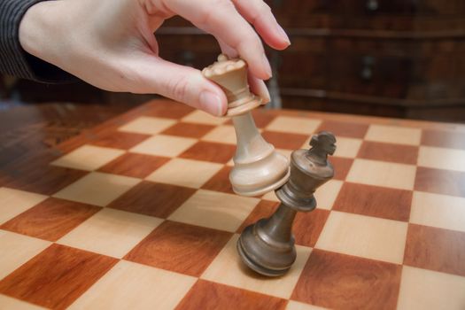 Concept: the woman who dominates the man. A woman's hand gives checkmate to the king with the queen on a wooden chessboard, with no other pieces in play