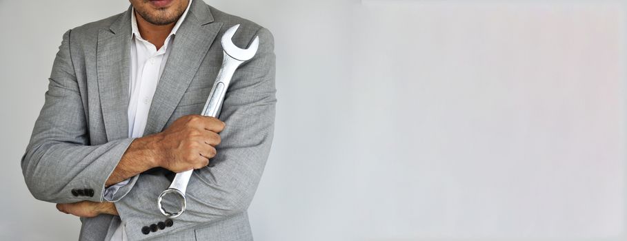 Man on grey suit. Man holding wrench on grey background with copy space.