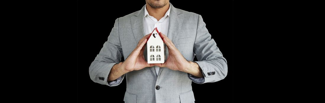 Home Concept : A man holding white mock up home on his hand for sale with  Copy space. Real estate agent with house model at Metal. Love home. New house. Renovate. Construction Building. Housing loan. Mortgage. Financial Agent. Property Investment. House Mortgage.