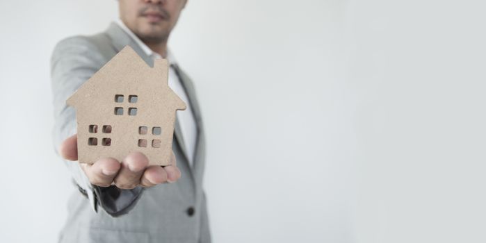 Home Concept : A man holding white mock up home on his hand for sale with  Copy space. Real estate agent with house model. Love home. New house. Renovate. Construction Building. Housing loan. Mortgage. Financial Agent. Property Investment. House Mortgage.