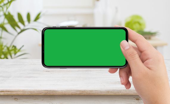 Isolated human right hand holding black mobile smart phone device mockup  green screen in kitchen 
