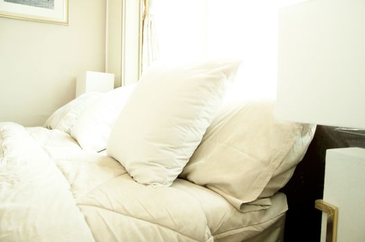 Bed maid-up with clean white pillows and bed sheets in luxury room. Close-up. Lens flair in sunlight.