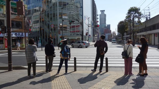 Tokyo, Japan - October 25, 2017 Tourist people with stand in front of crosswalk at the junction business street with car on the road (view from back)                                