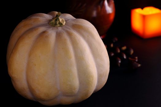 Pumpkin. Chestnuts and candle in background. Dark background