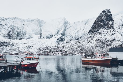 Ship fishing boat in Hamnoy fishing village on Lofoten Islands, Norway with red rorbu houses. With falling snow
