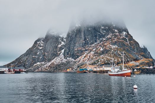 Ship fishing boat in Hamnoy fishing village on Lofoten Islands, Norway with red rorbu houses. With falling snow